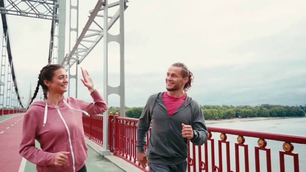 笑顔のランナーがお互いを見て、ジョギングし、橋の上に高い5を与える - 映像、動画