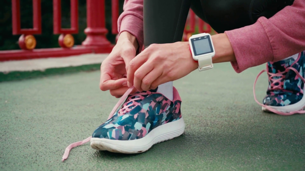 Cropped view of woman with smartwatch tying laces of sneaker on bridge - Filmmaterial, Video