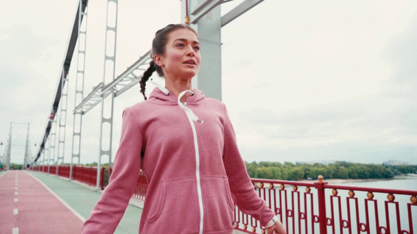 Усміхнена спортсменка стрибає на мосту з природним пейзажем на фоні
 - Кадри, відео