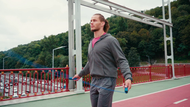Konzentrierter Sportler Seilspringen auf Brücke mit Bäumen im Hintergrund, Zeitlupe - Filmmaterial, Video