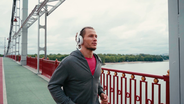 Sportman met koptelefoon joggen op brug met natuur landschap op de achtergrond - Video
