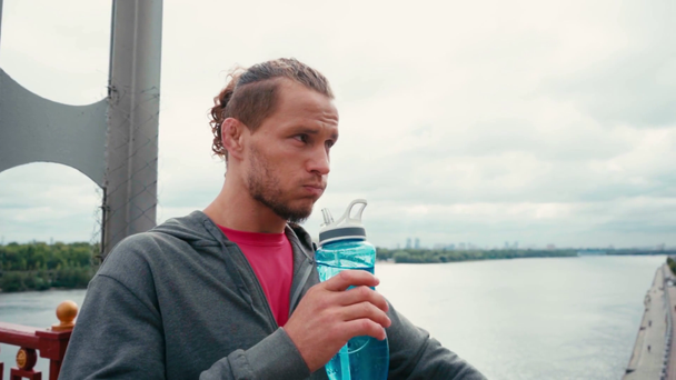 Sportman drinkwater uit sportfles op brug met natuur op achtergrond - Video