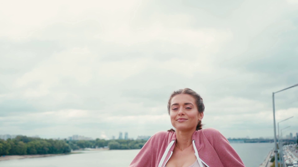 Glimlachende sportvrouw met gesloten ogen staande met bewolkte lucht op de achtergrond - Video