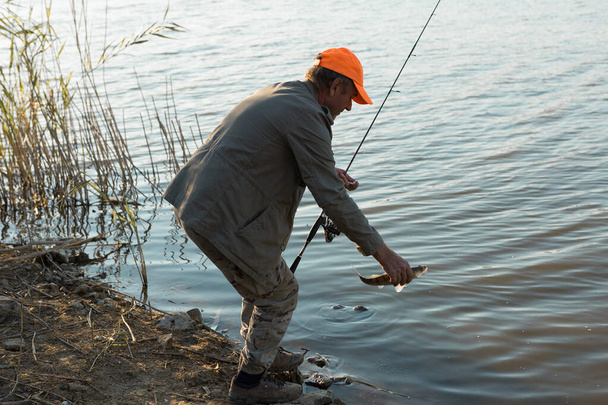 Ψαράς στέκεται στην όχθη του ποταμού και προσπαθεί να πιάσει ένα ψάρι. Αθλητισμός, αναψυχή, τρόπος ζωής. - Φωτογραφία, εικόνα
