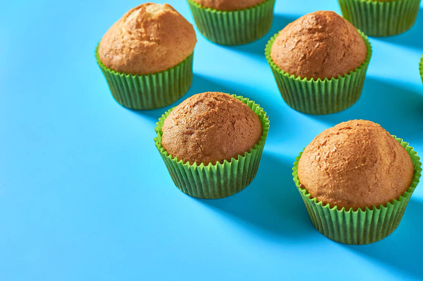 Many fluffy muffins in green paper molds scattered on blue background. Space for text - Fotoğraf, Görsel