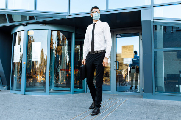 Man businessman in business clothes and a medical protective mask on his face, against the background of a glass office building - Fotografie, Obrázek