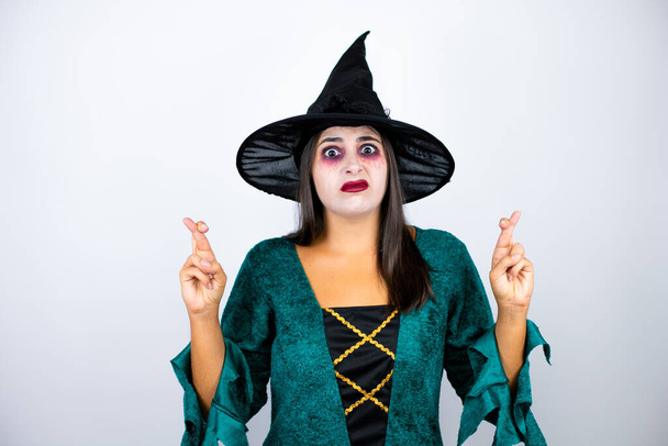 Kobieta w kostiumie czarownicy na białym tle gestykulujący palec skrzyżowany uśmiechając się z nadzieją i patrząc z boku - Zdjęcie, obraz