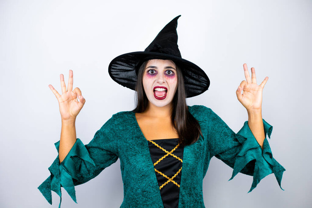 Žena na sobě čarodějnice kostým přes izolované bílé pozadí dělá v pořádku znamení s prsty a usmívá se, vynikající symbol - Fotografie, Obrázek
