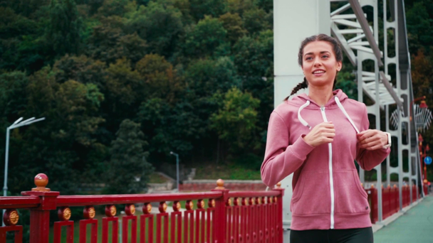 Lachende sportvrouw met smartwatch draait op brug met de natuur op de achtergrond - Video