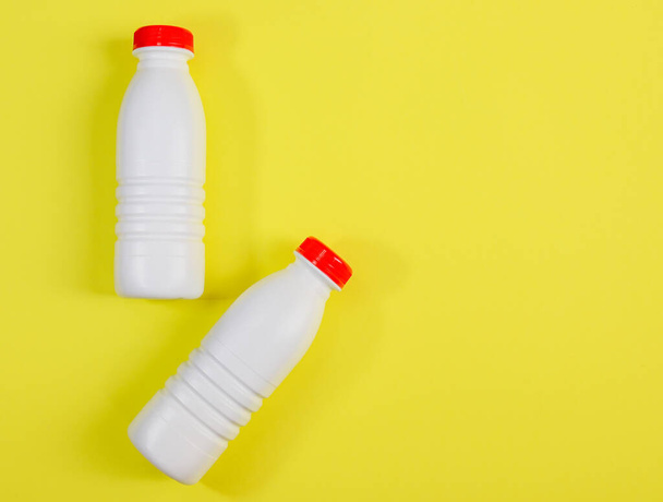 flessen op gele achtergrondTwee witte plastic flessen met rode dop liggen links tegen een gele achtergrond met ruimte voor tekst rechts, bovenaanzicht close-up. - Foto, afbeelding
