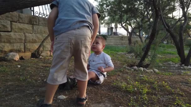 Bonito 4 anos de idade ajudando seu irmão a limpar o joelho depois que ele se sentiu para baixo. Irmãos cuidando uns dos outros - Filmagem, Vídeo