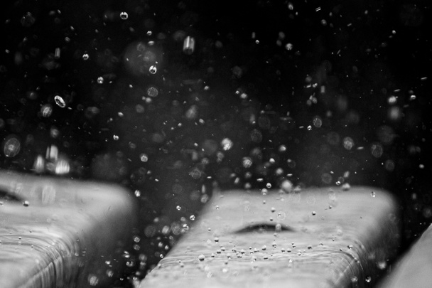 close-up de gotas de lluvia cayendo sobre el banco de un parque en blanco y negro - Fotografie, Obrázek