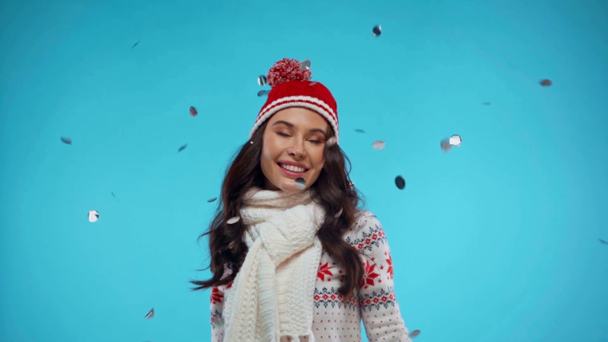 Happy young adult woman in warm clothing, throwing confetti on blue - Metraje, vídeo