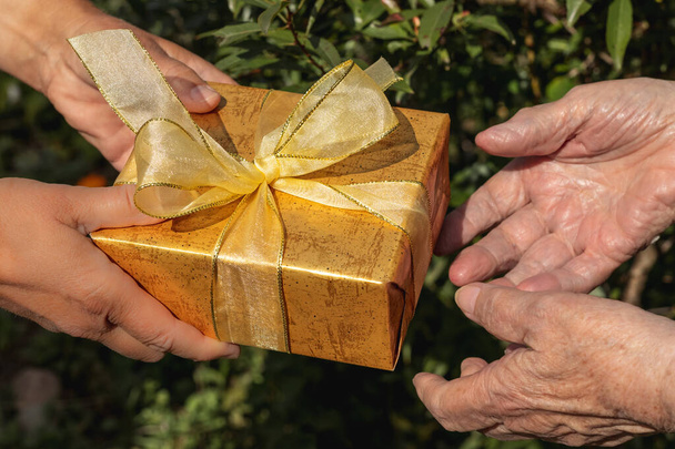 Az ajándékdoboz odaadása a nagymamának. Ajándék doboz és a nagymama keze. - Fotó, kép