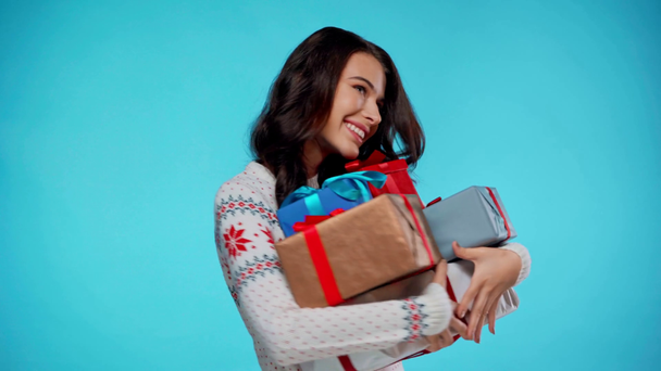 Happy young adult woman holding bunch of gift boxes on blue background - Footage, Video