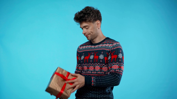 Ongelukkig jong volwassen man overgeven geschenkdoos, glimlachen, kijken naar camera op blauw - Video