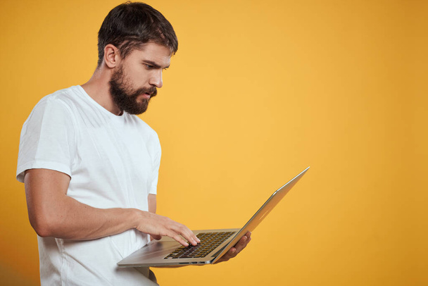 Un uomo con la barba tiene in mano un computer portatile su una tastiera di sfondo giallo monitor nuove tecnologie vista laterale - Foto, immagini