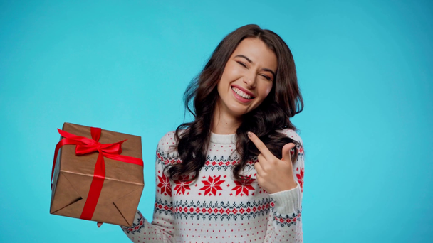 Happy young adult woman holding and pointing with finger at gift box on blue - Footage, Video