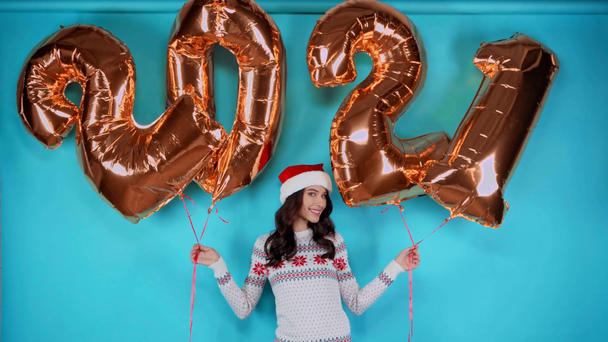 jong volwassen vrouw in santa hoed met gouden ballonnen met nummers op blauw - Video