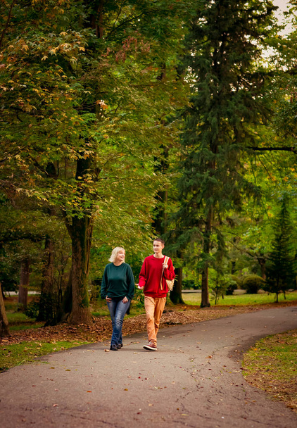 Mooie vrouw, blond, middelbare leeftijd, met een tiener zoon wandelen in het park, een mooie herfstdag - Foto, afbeelding