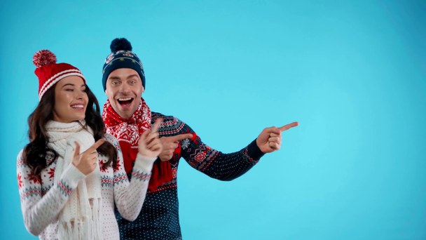 Excited couple in hats and scarfs pointing with fingers on blue - Footage, Video
