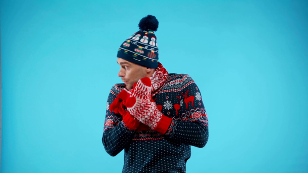 Giovane uomo adulto in vestiti caldi congelamento, strofinando palme e braccia su blu - Filmati, video