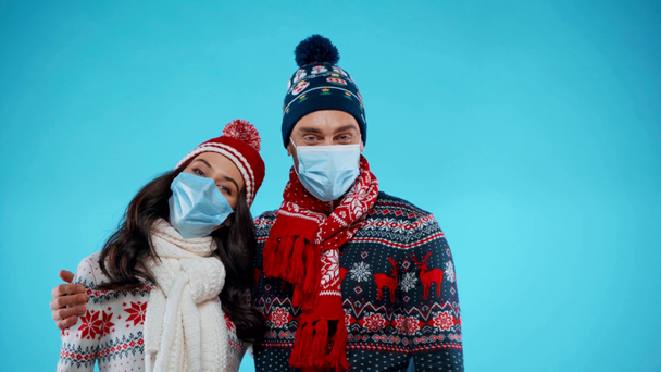 Young couple in warm clothes and medical masks embracing on blue - Footage, Video