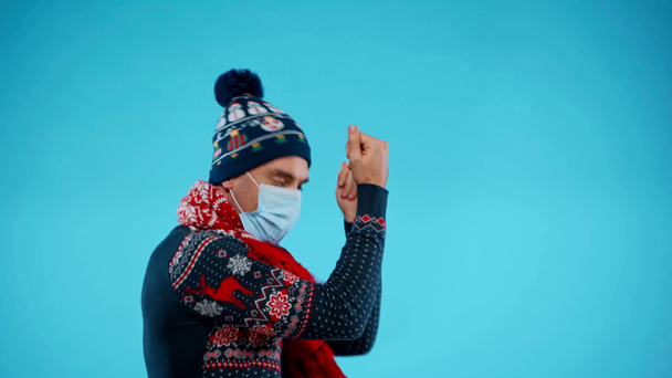暖かい服を着た精力的な男は踊り、青い上に医療マスクを身に着けています - 映像、動画