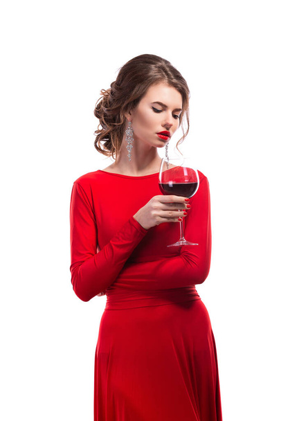 Woman with makeup, hairstyle waering red dress posing with glass of vine over white background, isolate - Foto, imagen