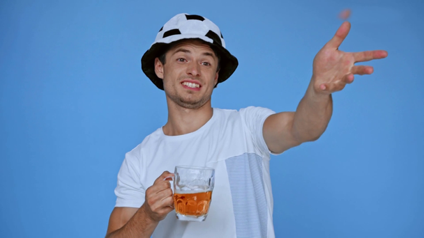 heyecanlı futbol fanatiği şapka jestleri yapıyor ve mavi üzerine izole bira içiyor - Video, Çekim
