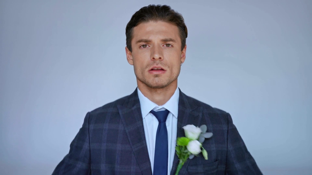 Bräutigam fixiert Haare, Jacke und Krawatte, während er isoliert auf grau in die Kamera blickt - Filmmaterial, Video