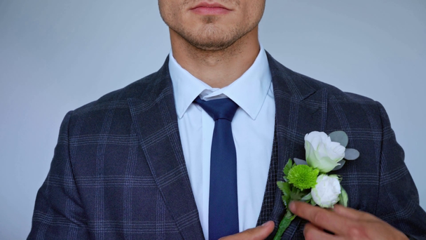 cropped view of groom fixing suit and boutonniere isolated on grey - Πλάνα, βίντεο