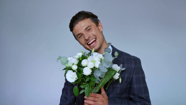 Χαρούμενος γαμπρός κρατώντας λουλούδια και μιλώντας απομονωμένος στο γκρι - Πλάνα, βίντεο