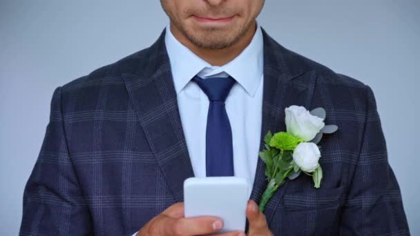 vista recortada de las pruebas de novio feliz en el teléfono inteligente aislado en gris - Imágenes, Vídeo