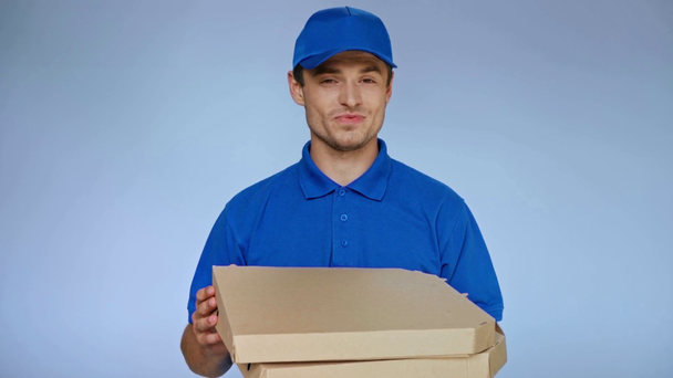 happy delivery man holding and smelling carton pizza boxes on grey - Materiał filmowy, wideo
