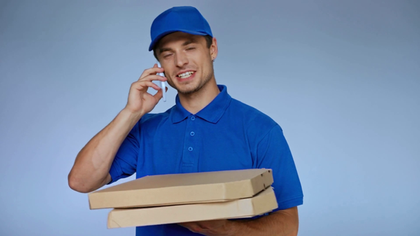 szczęśliwy dostawca trzyma pudełka kartonowe z pizzą i rozmawia na smartfonie na szarym - Materiał filmowy, wideo