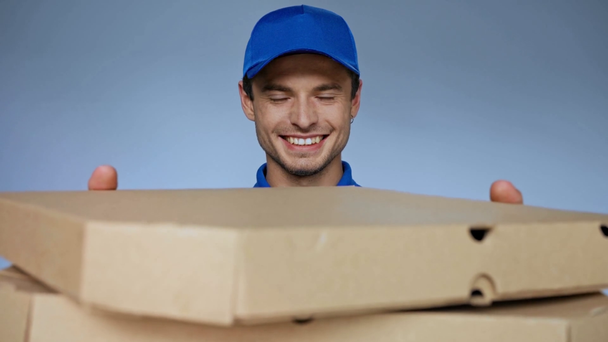 Gülümseyen teslimatçı şapkalı adam gri kutuda pizza kutuları tutuyor. - Video, Çekim