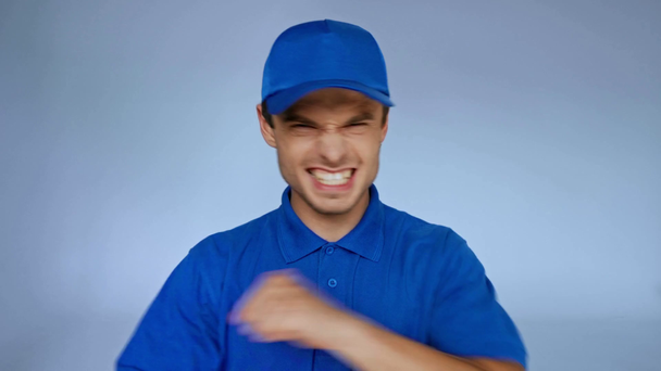 allegro uomo di consegna in berretto blu gesticolando sul grigio - Filmati, video