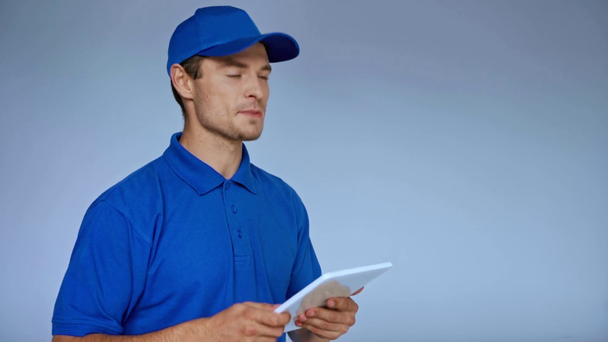 dodávka muž v čepici pomocí digitálního tabletu při objednávce na šedé - Záběry, video