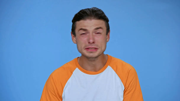 upset man rubbing eyes and wiping tears while crying isolated on blue - Footage, Video