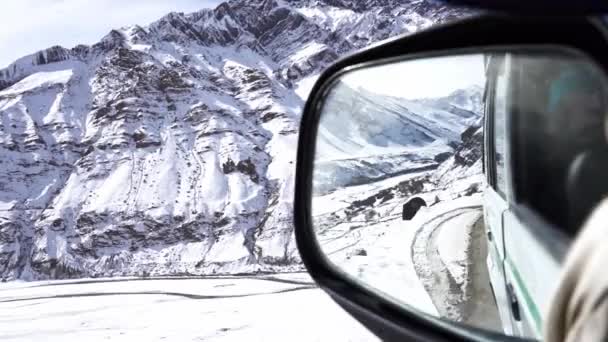Achteraanzicht spiegelperspectief van een auto in ruw bergachtig terrein tijdens winters - Video