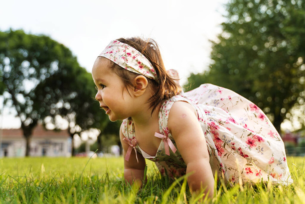 One small caucasian baby girl sitting on the grass wearing dress in the field in summer or autumn day smiling happy having fun crawling - childhood concept - Photo, Image