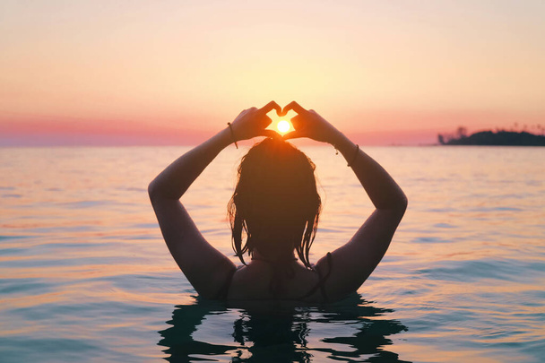 Widok z tyłu na azjatycką kobietę robiącą znak serca w morzu. Wakacje witalność zdrowego stylu życia. Sylwetka ręka w kształcie serca. - Zdjęcie, obraz