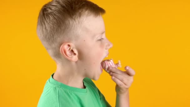 Divertido niño comiendo sabroso donut sobre fondo de color - Metraje, vídeo