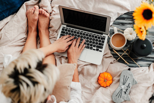 Woman is enjoying coffee in the bed. Working on the laptop. Sunflower arrangement. Bedroom vibe. Autumn season. Feeling home comfortable. Enjoying little things. Fall colors and mood. Work at home. - Foto, Bild