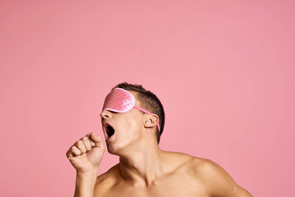 man in pink sleep mask on pink background naked shoulders morning - Foto, Bild