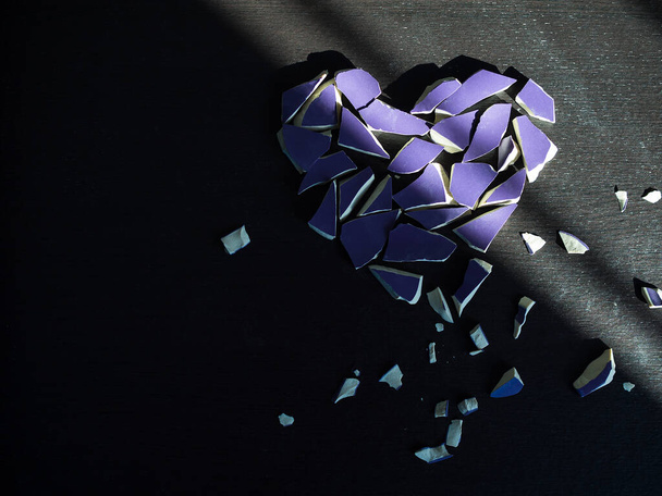 Concepto de corazón roto. Cristal roto púrpura sobre fondo negro oscuro con sombra clara. - Foto, Imagen