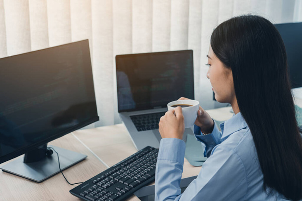 Mulher asiática estava bebendo café no início da manhã enquanto contemplava o programa e o código na tela do computador. - Foto, Imagem