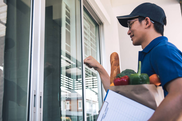 Азиатский мужчина, держащий пакет с едой, стучащий в дверь.. - Фото, изображение