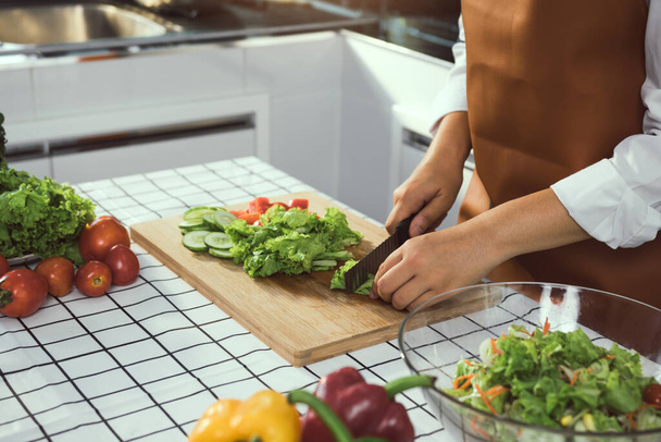 Asian woman uses a knife to cut the salad greens in the kitchen. - Photo, Image